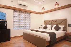 Un dormitorio con cama, televisor, ventana con persianas y equipo de aire acondicionado.