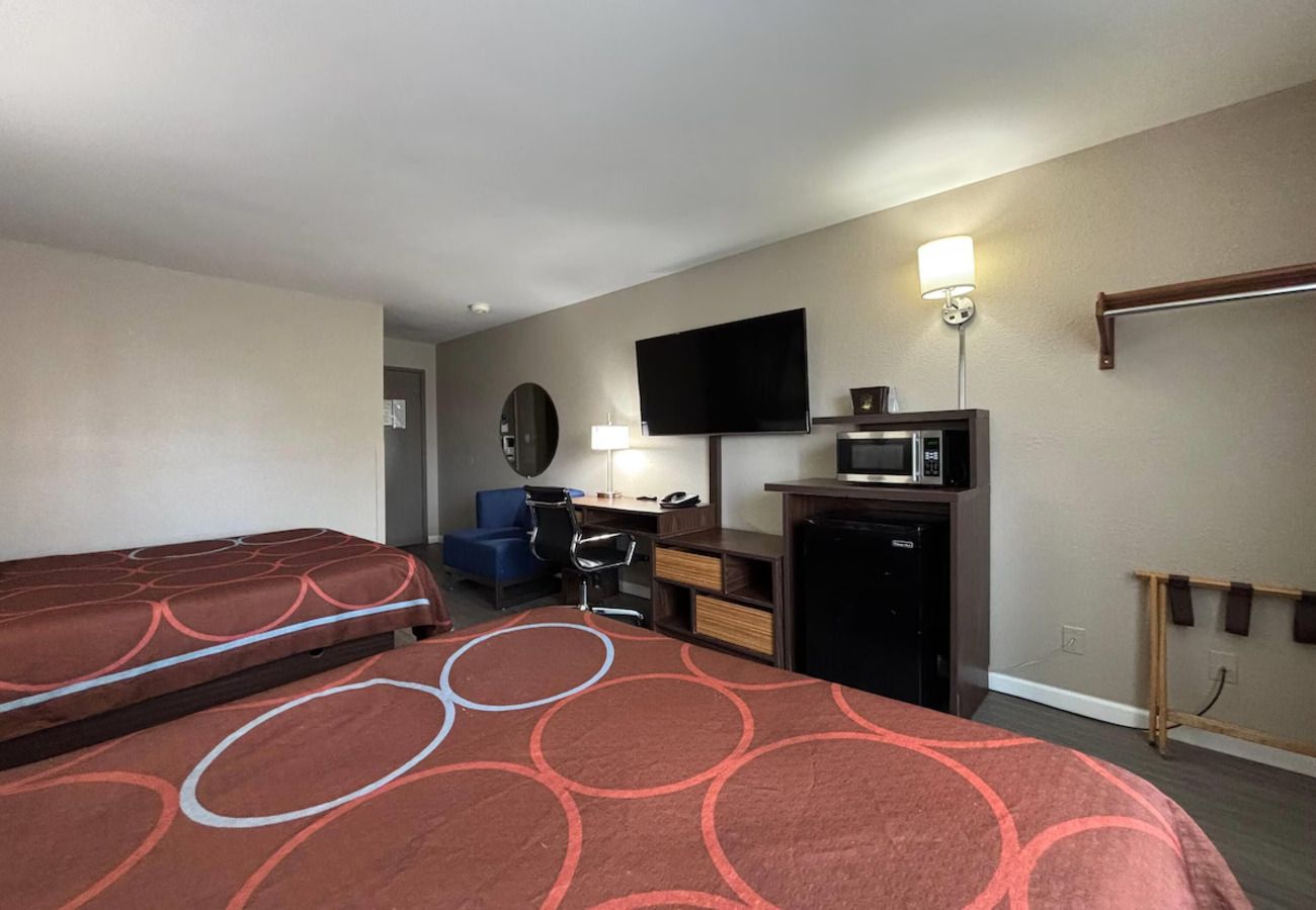A hotel room with two beds, a desk, a chair, a television, a microwave, and a small refrigerator.