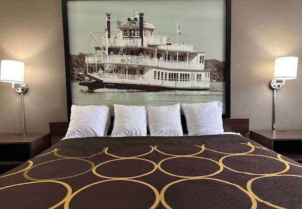 A hotel room with a bed, two bedside lamps, a framed picture of a boat on the wall, and a patterned bedspread. - amerivu inn & suites alton (Alton)