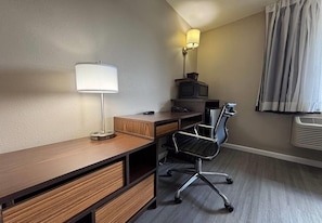 Une chambre d’hôtel avec un bureau en bois, un fauteuil de bureau noir, une lampe, un téléviseur et une fenêtre avec des rideaux.