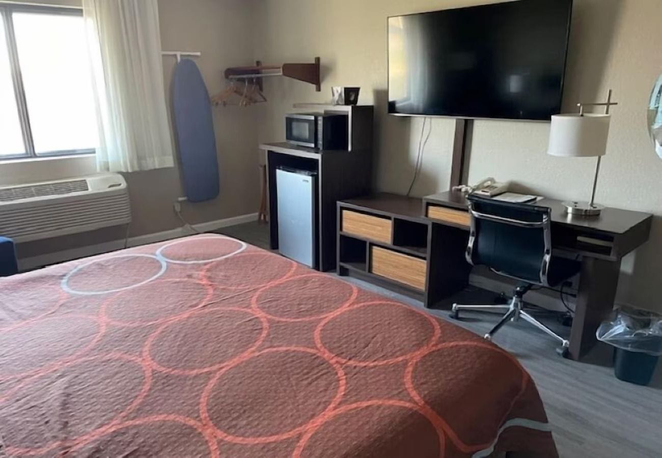 A hotel room with a bed, a desk with a computer, a television, and a microwave.