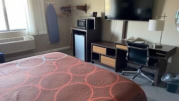 A hotel room with a bed, a desk with a computer, a television, and a microwave.