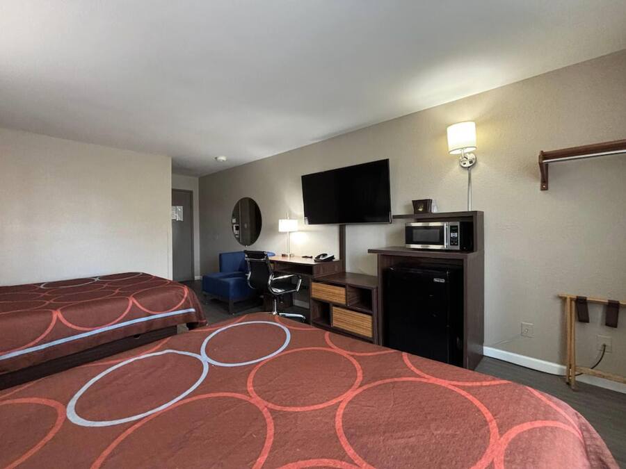 Habitación de hotel con dos camas, un escritorio, una silla, un televisor, un microondas y un refrigerador pequeño.