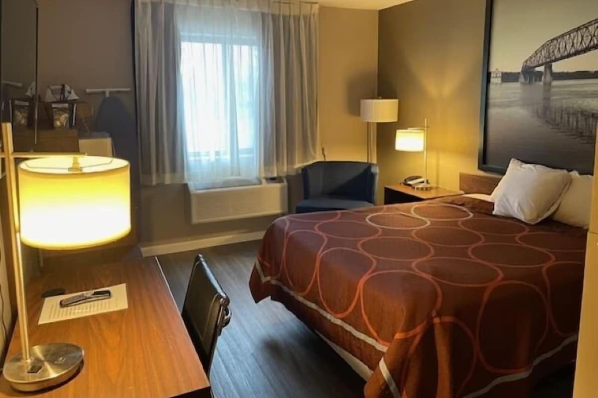 A hotel room with a bed, a desk, a chair, a lamp, and a window with curtains.