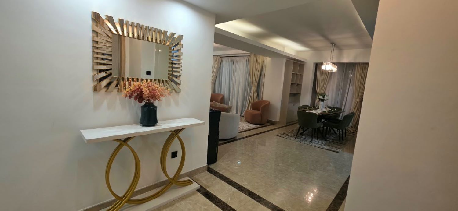 A modern interior with a white console table, a decorative mirror, and a dining area with a chandelier.