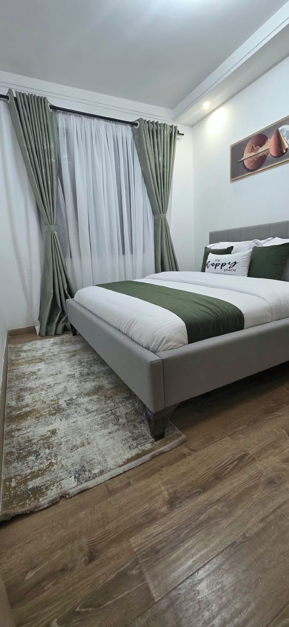 A bedroom with a bed, curtains, a rug, and a wall-mounted picture.