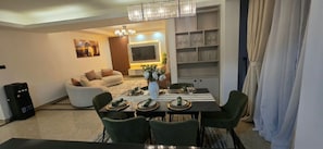 Uma sala de jantar com mesa posta para quatro pessoas, um sofá, uma TV e uma estante de livros.