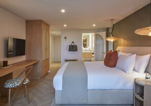 A hotel room with a bed, bedside table, a desk with a chair, a television, and a bathroom visible through an open door. - Casa Luma (Cape Town)