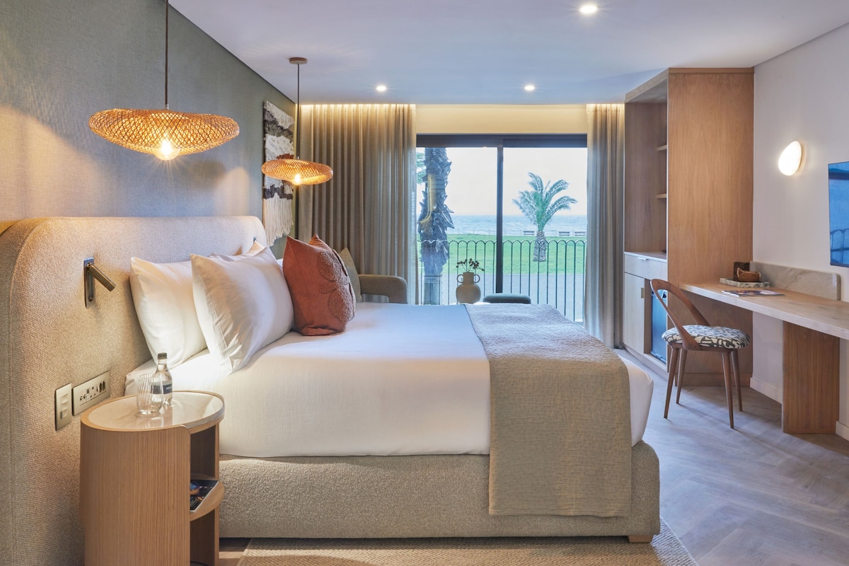 A modern hotel room with a large bed, a desk, and a balcony with a view.