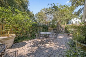 Ein Patio mit rundem Tisch und Stühlen, umgeben von einem Holzzaun und üppiger Bepflanzung.