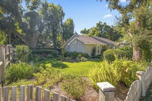 A house with a well-maintained lawn, surrounded by a wooden fence and various plants. - Great 3 bedroom 3 bath single story house near Pier/Village and the beach (Saint Simons Island)