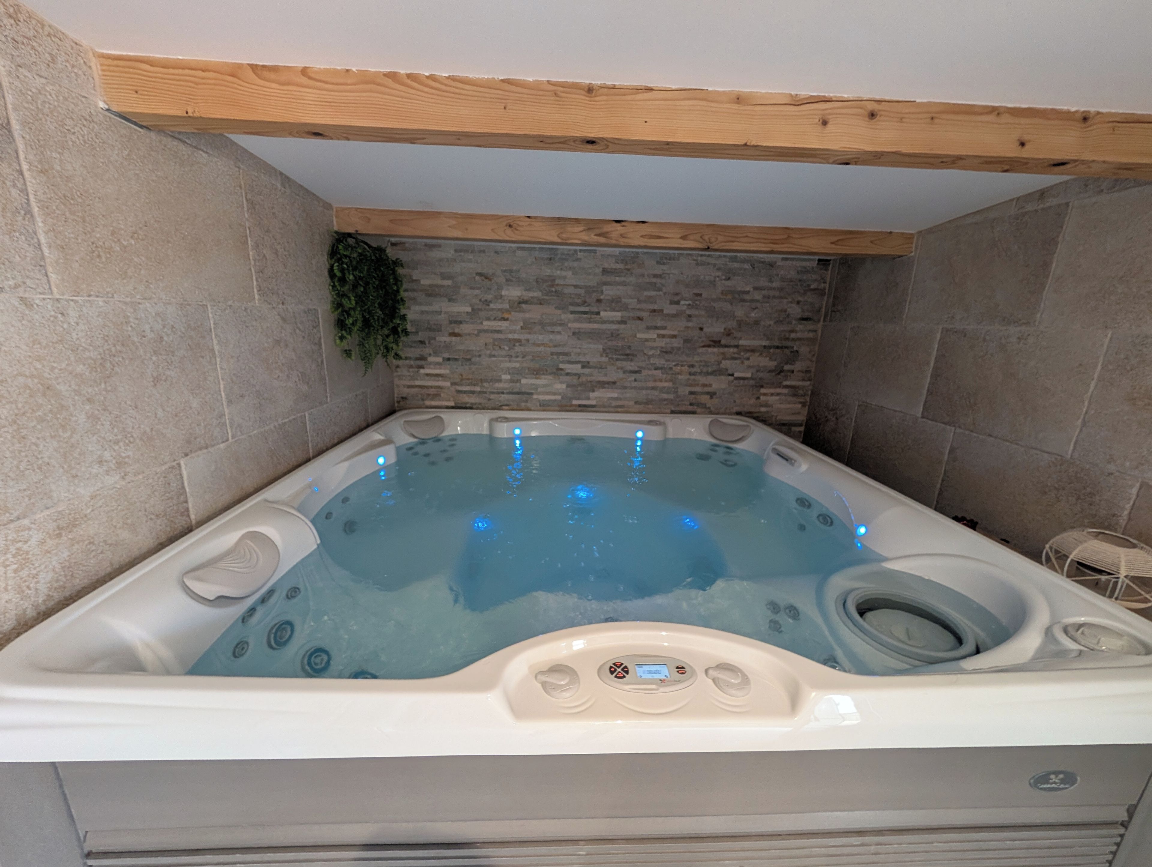 Ein Whirlpool mit Bedienfeld, umgeben von Steinwänden und einer Holzbalkendecke.