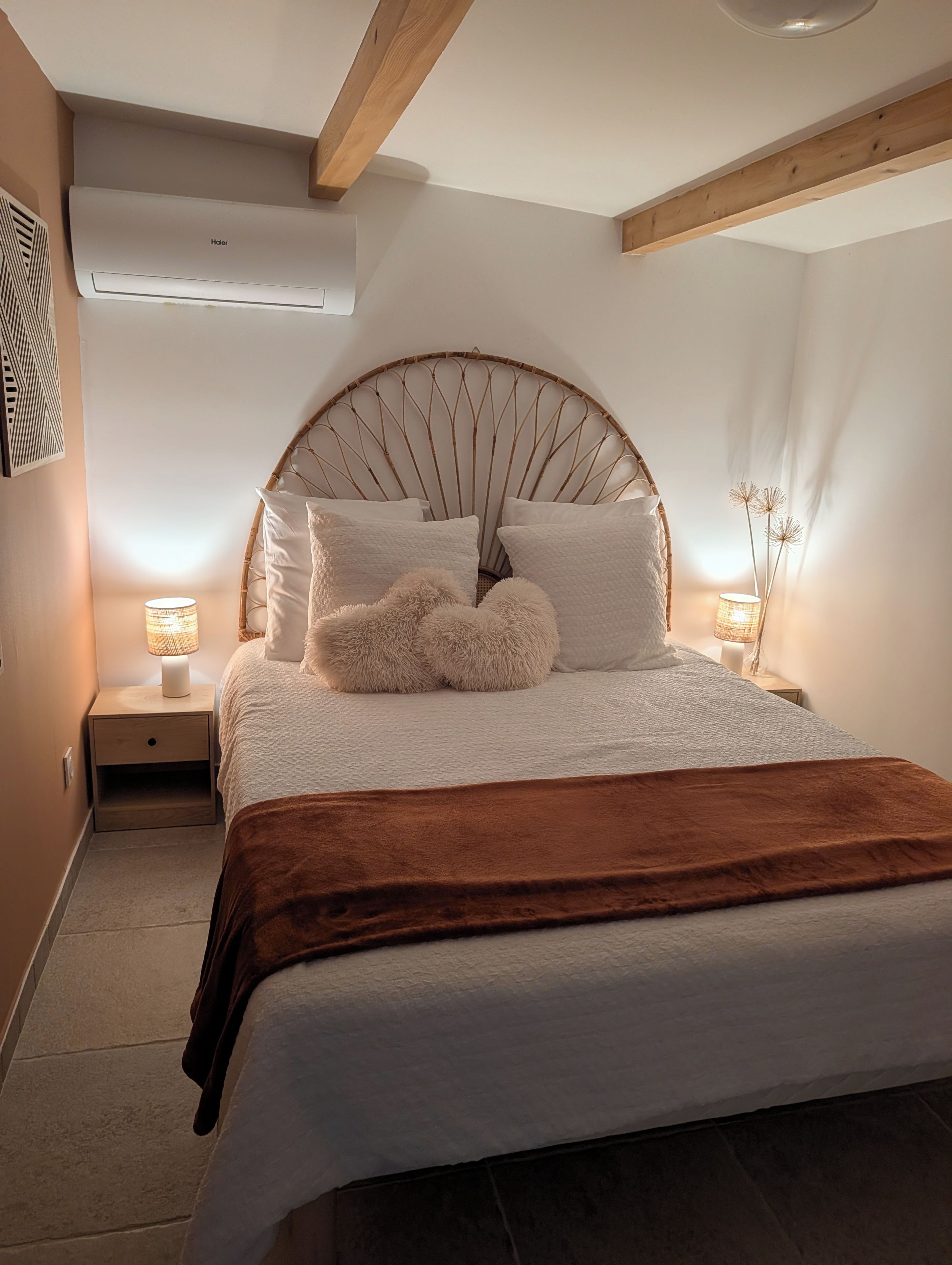 A bedroom with a large bed, a headboard, bedside lamps, and a wall-mounted air conditioner.