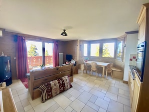A cozy living room with a sofa, a dining table with chairs, and a kitchen area with cabinets and a refrigerator. - A201 - 57 m² - 3-room apartment - 6 people (Prapoutel)