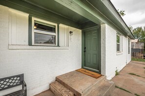 A white brick house with a green door, a window, and a small front porch with steps. - Aesthetic 3BR Home w/ Coffee Bar & Large Yard (Abilene)