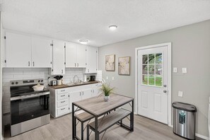 A modern kitchen with white cabinets, a stainless steel oven, and a wooden table. - Aesthetic 3BR Home w/ Coffee Bar & Large Yard (Abilene)