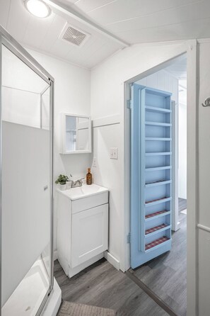 Une salle de bain avec un lavabo blanc, un miroir et un meuble de rangement bleu doté d’étagères.