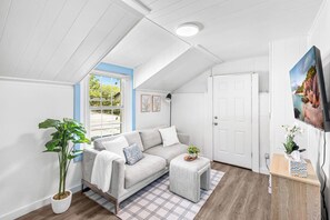A modern living room with a sofa, a small table, a potted plant, and a door leading to another room. - Private 1BR Guest Suite with Deck & Full Kitchen (Abilene)