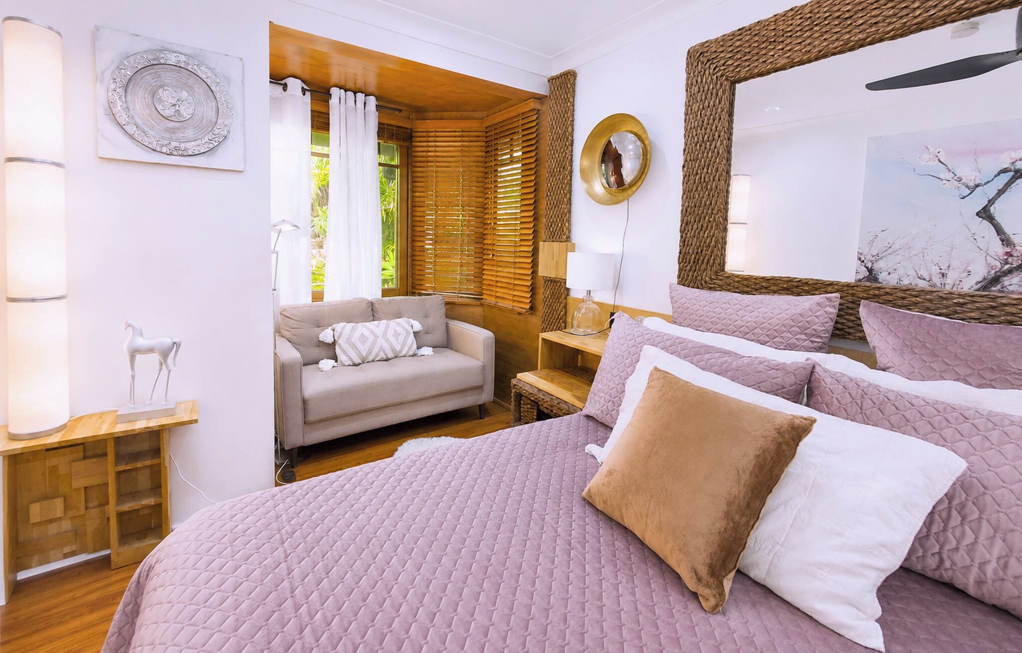 Een slaapkamer met een groot bed, een bank, een houten vloer en een raam met jaloezieën.