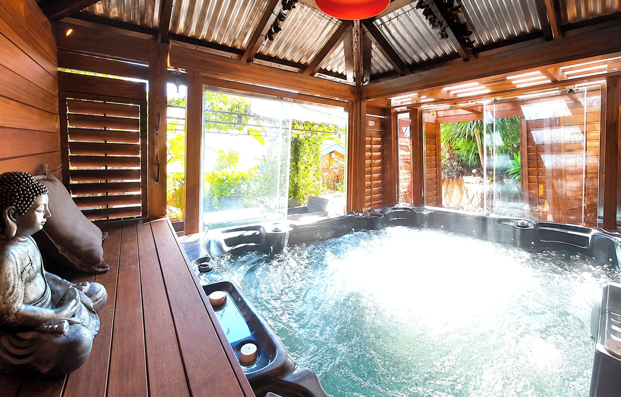Un bain à remous avec une terrasse en bois et une statue de Bouddha.