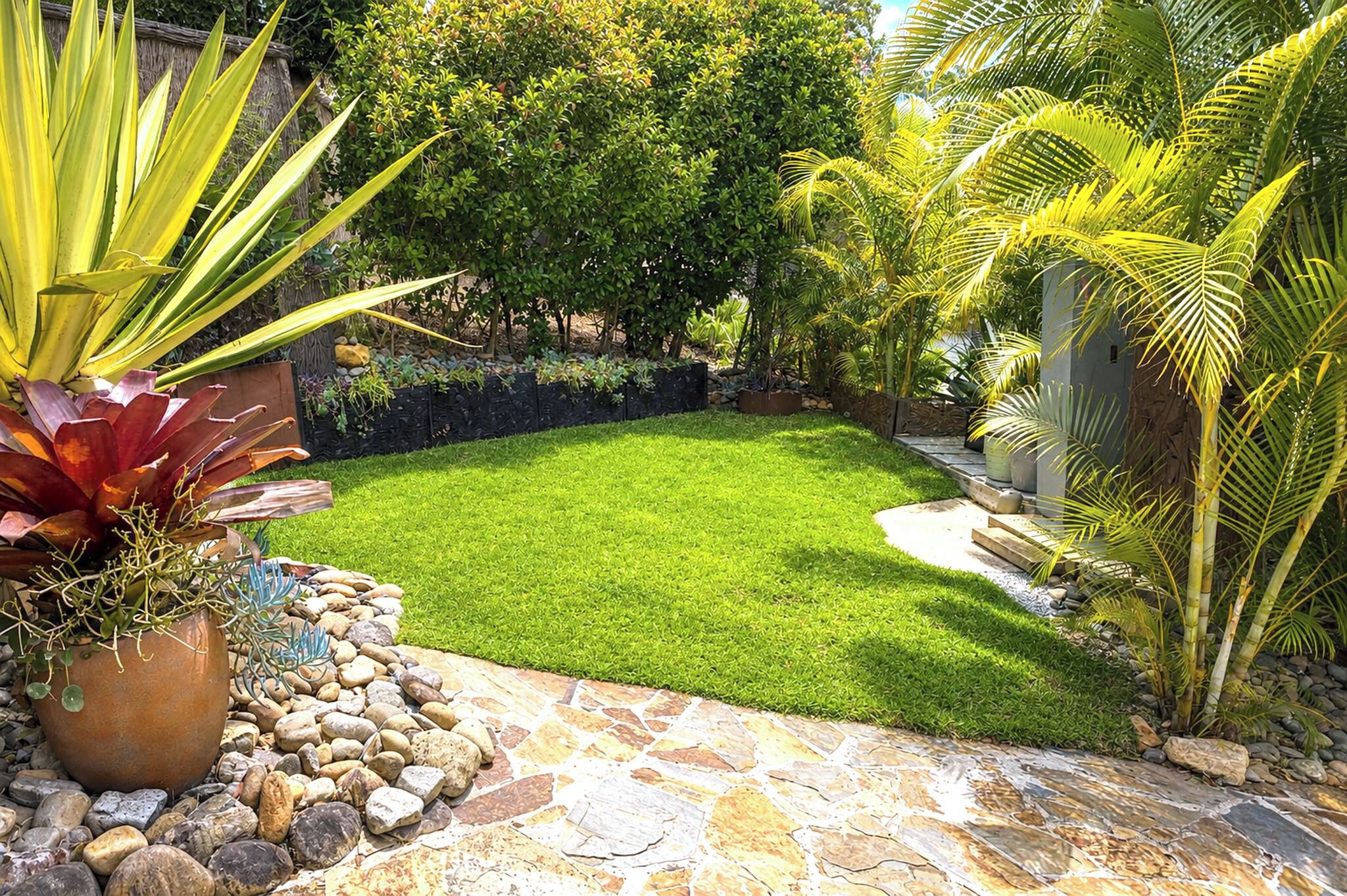 Un jardin bien entretenu, avec une variété de plantes, un chemin de pierres et une pelouse soigneusement taillée.