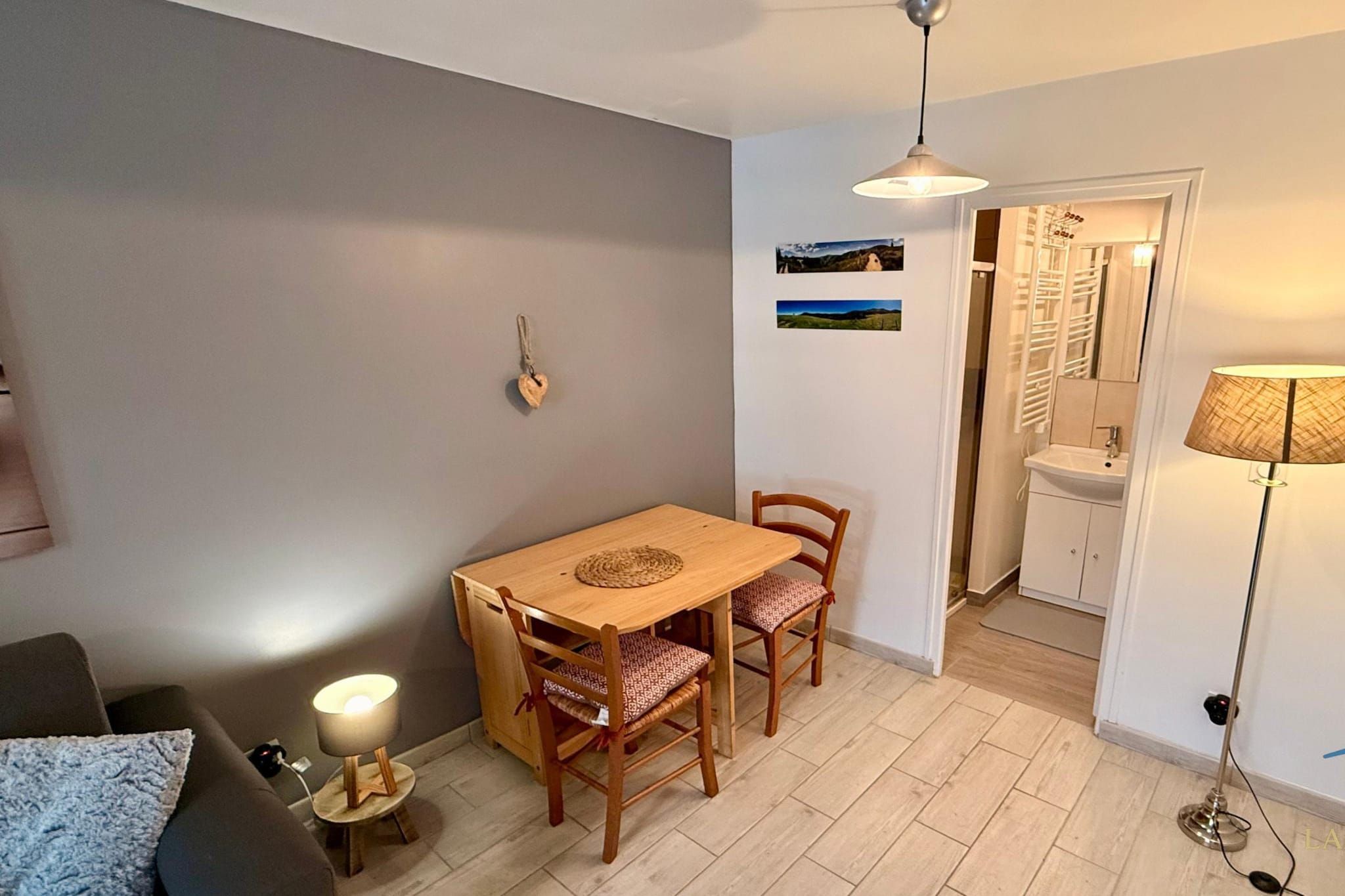 A compact living space with a dining area, a sofa, a lamp, and a view into a bathroom.