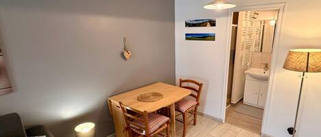 A compact living space with a dining area, a sofa, a lamp, and a view into a bathroom.