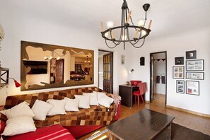 A living room with a checkered sofa, a dining area with a red chair, and a chandelier. - Country House 'Finca Fani 1 con Estudio' with Sea and Mountain Views, Pool, Wi-Fi, Terrace and Garden (Los Corralillos)