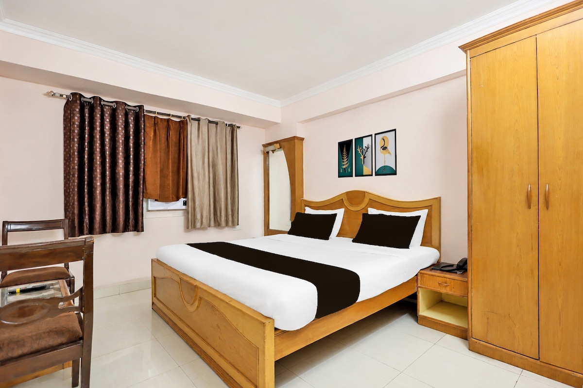 A hotel room with a wooden bed, a nightstand, a wardrobe, a chair, and a window with curtains.