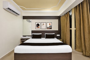 A hotel room with a large bed, a bedside table, a nightstand, a wall-mounted air conditioner, and a window with curtains. - Townhouse City Centre Gwalior (Gwalior)