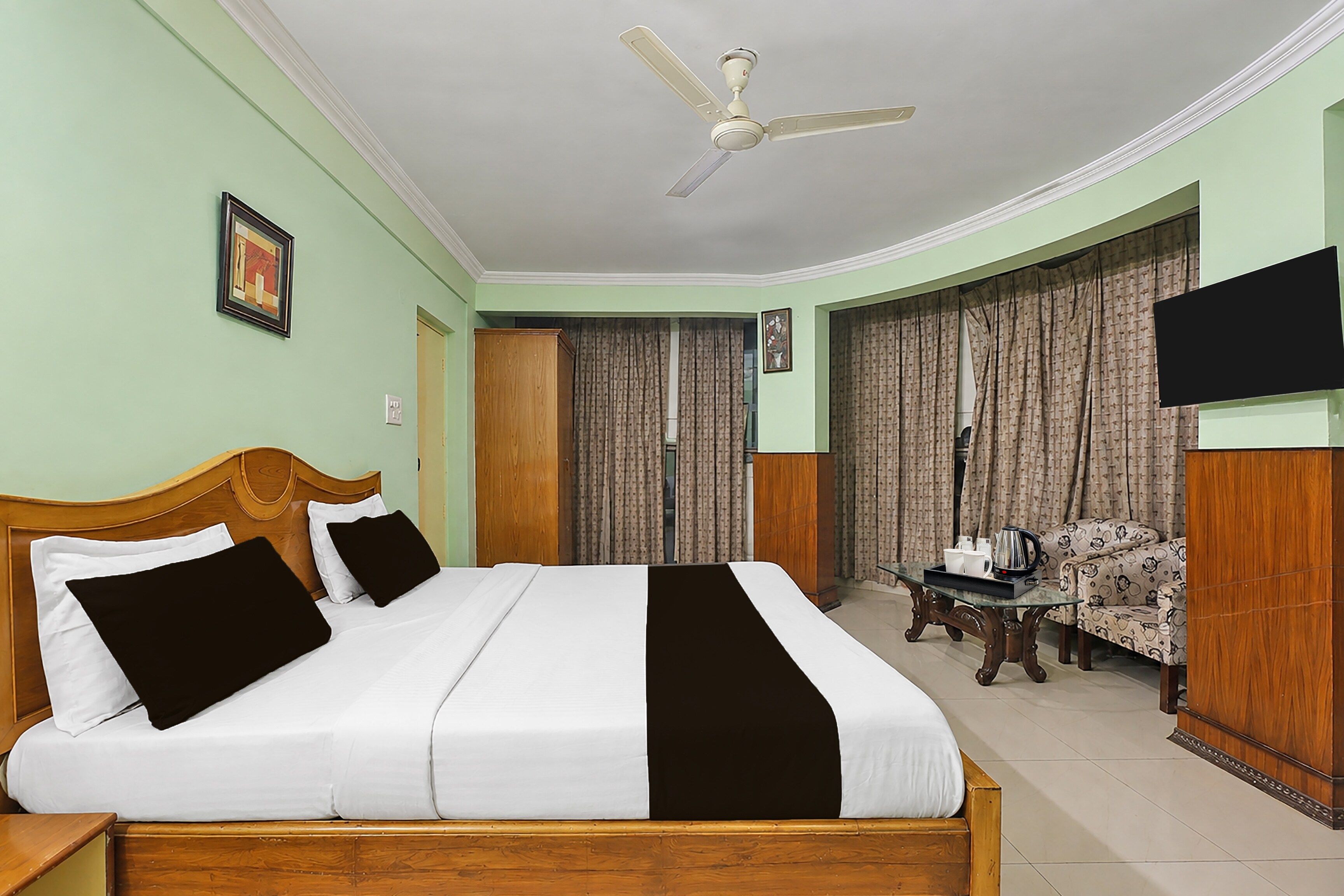 A hotel room with a bed, a ceiling fan, a television, curtains, and a coffee table.