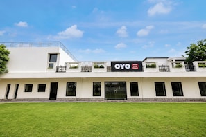 Et moderne hotel med fladt tag, flere balkoner og et skilt med teksten 'OYO Hotel Amara Palace'.
