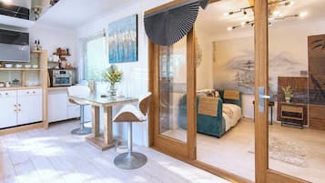 A modern kitchen with a dining area, a sliding glass door leading to a bedroom with a bed and a view of a mountain.