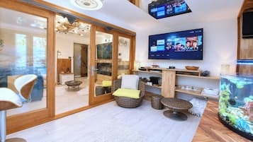 A modern living room with a flat-screen TV mounted on the wall, a large fish tank, and a sliding glass door leading to a dining area.