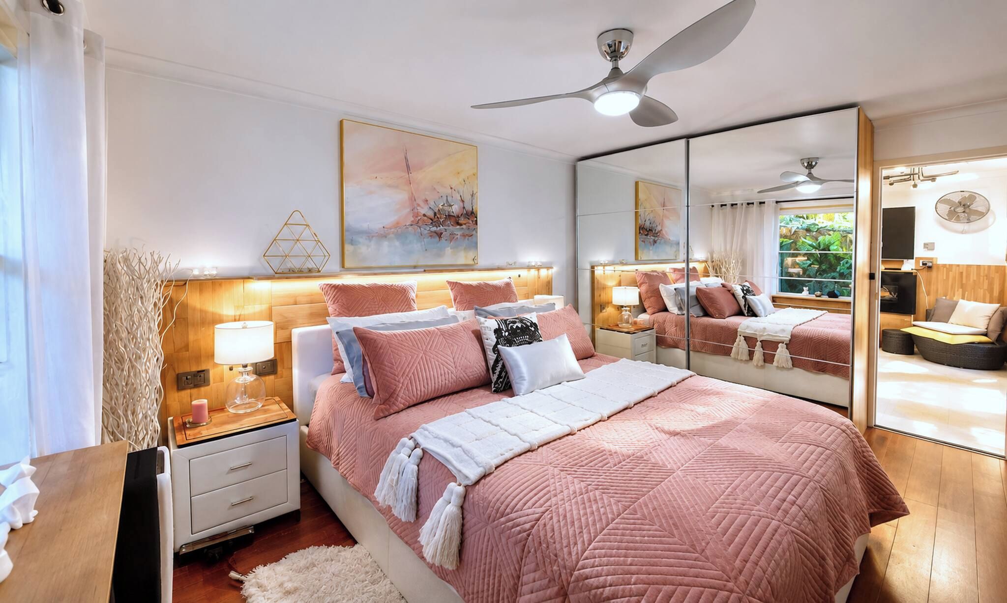 A bedroom with a large bed, bedside tables, a mirror, and a ceiling fan.