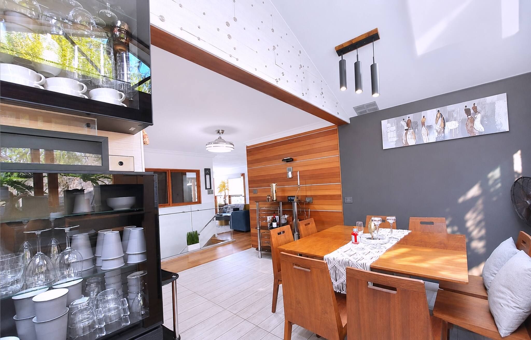 Une cuisine moderne avec un coin repas, comprenant une table en bois, des chaises et un buffet en verre contenant de la vaisselle.