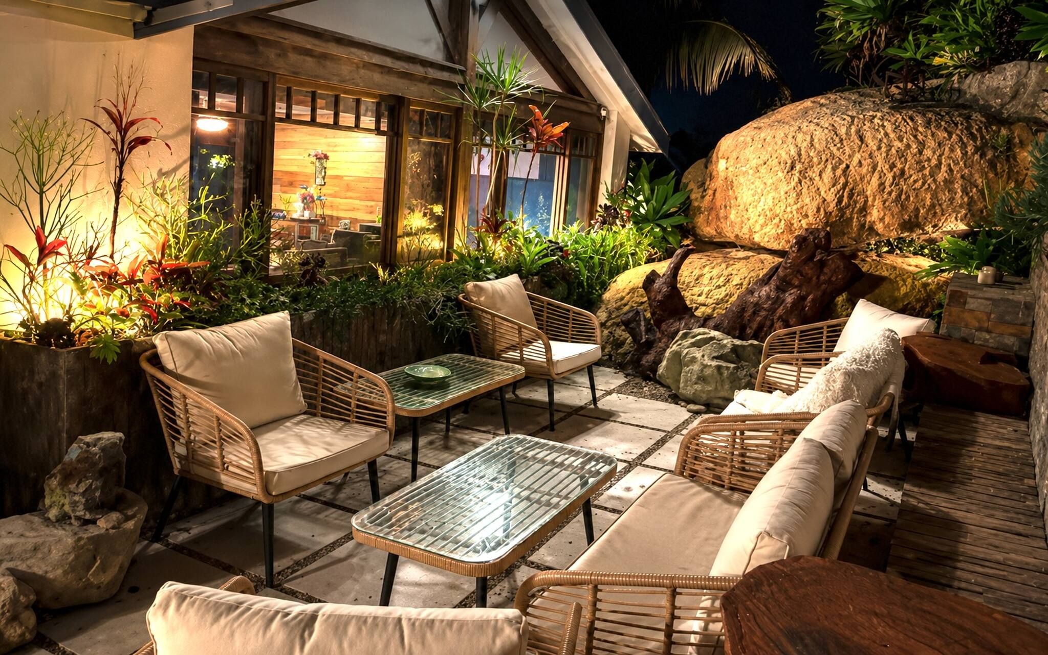 An outdoor seating area with wicker furniture, a glass table, and tropical plants.
