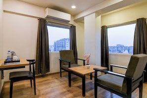 Une chambre d’hôtel avec un plancher en bois, deux chaises, une petite table et une fenêtre avec des rideaux.