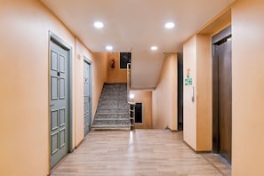 Un pasillo con una escalera que sube a un piso superior, puertas a ambos lados y un letrero de salida de incendios.