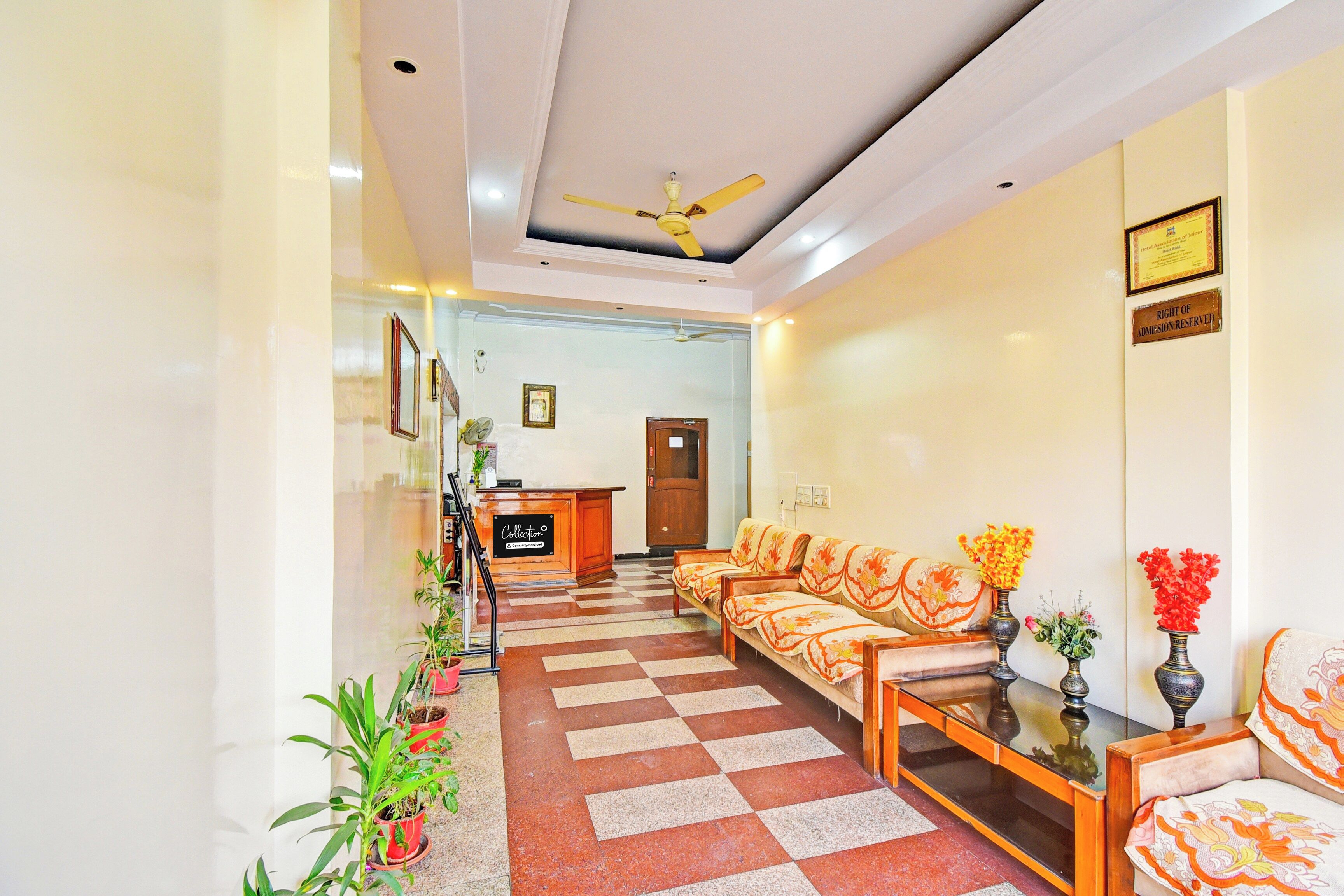 A hotel reception area with a checkered floor, a reception desk, a seating area with sofas, and a ceiling fan.