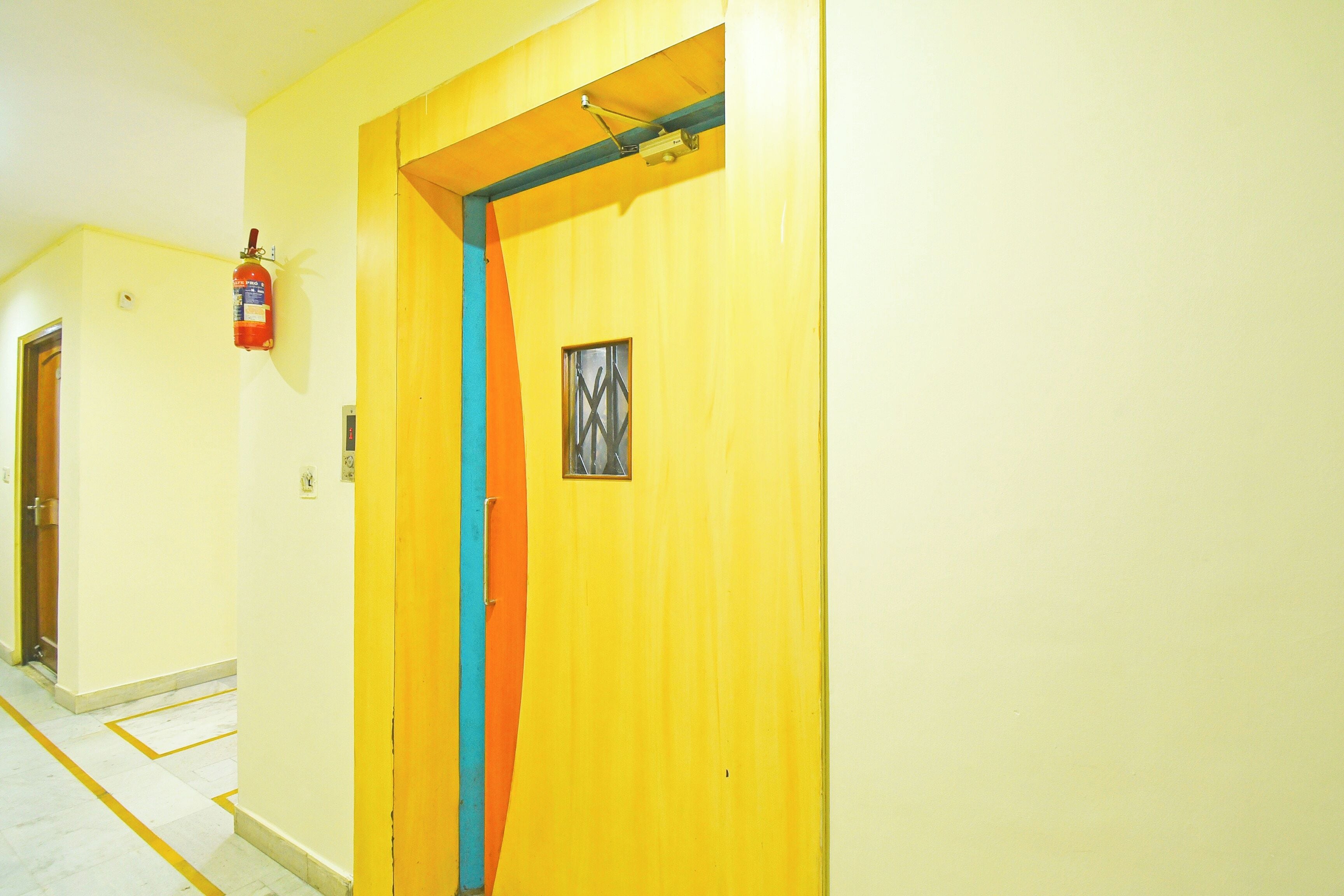 A hallway with a yellow door, a fire extinguisher, and a small window.