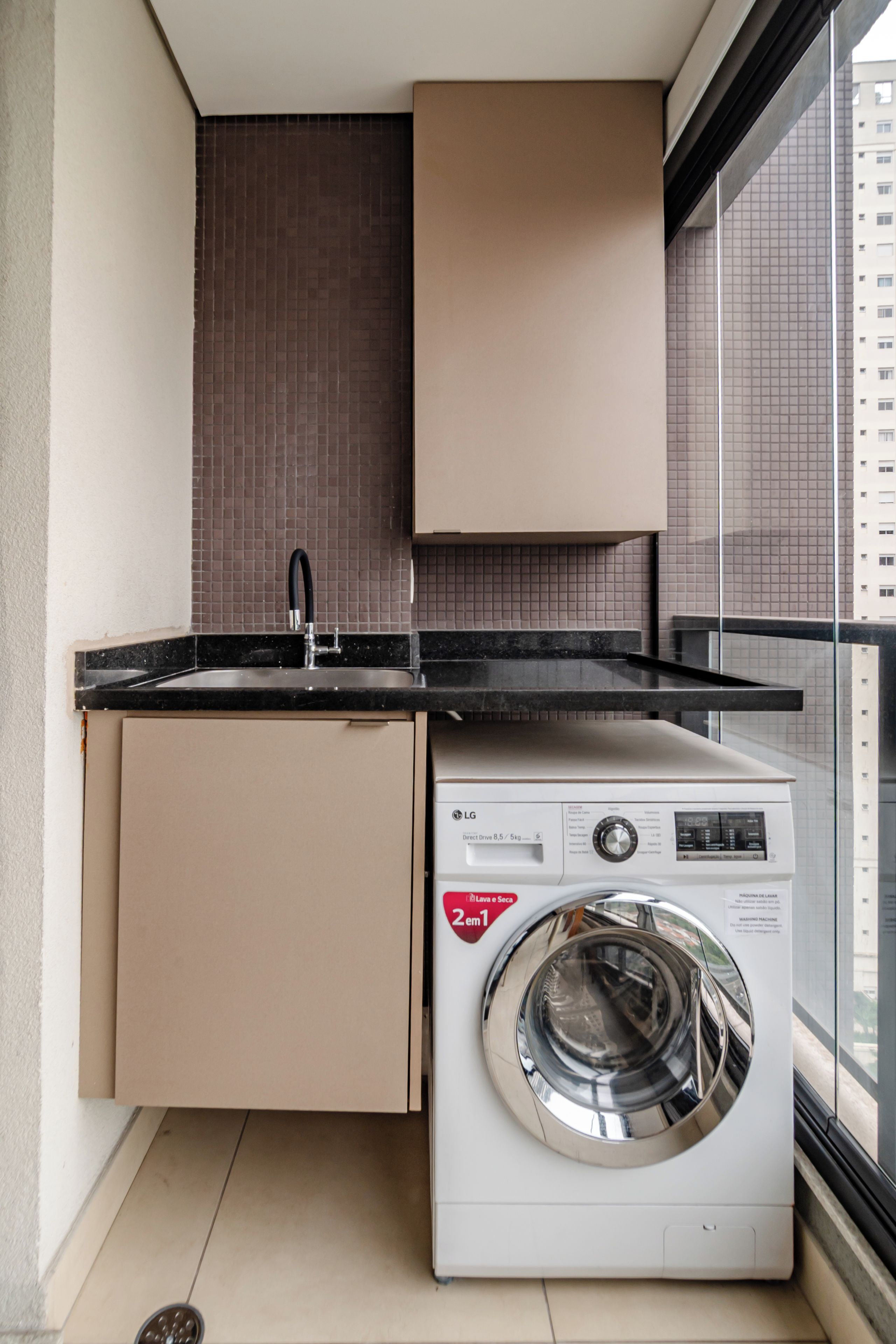 A compact laundry room with a washing machine and a sink, featuring a tiled backsplash and a window with a view of a building.