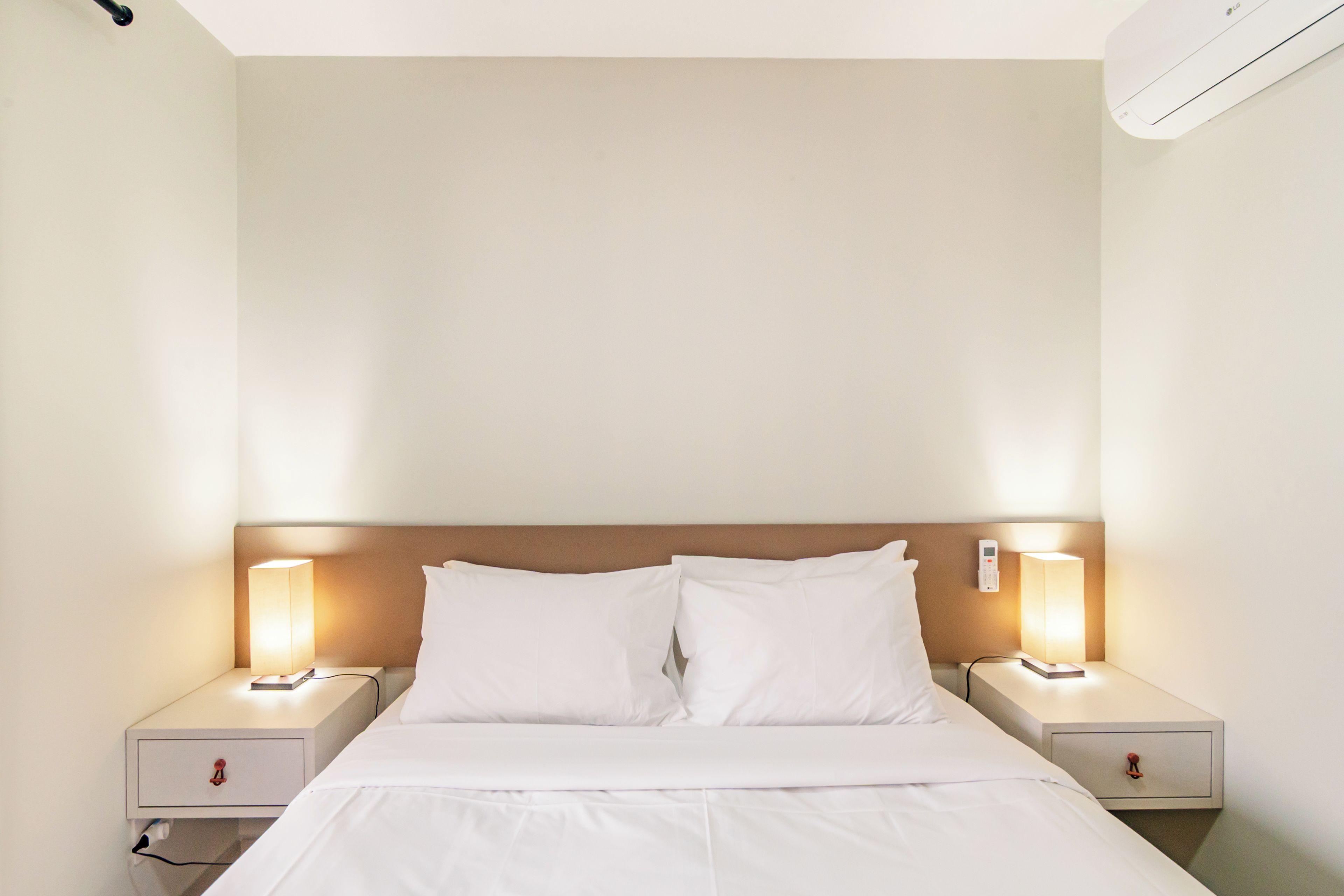 A hotel room with a single bed, two bedside tables, and a wall-mounted air conditioner.