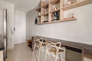 A modern kitchen with a built-in refrigerator, a coffee maker, and a wooden dining table with chairs. - Gabriele by Bhomy (São Paulo)