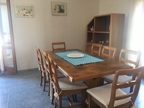 A dining area with a wooden table, six chairs, a blue placemat, and two wall-mounted pictures. - Casa Nene' Calasetta (Calasetta)