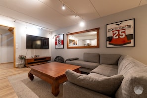 Ein Wohnzimmer mit einer Couch, einem Couchtisch, einem Fernseher und gerahmten Sportmemorabilien an der Wand.