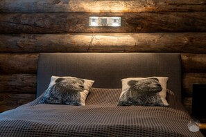 Ein schlafzimmer im Blockhausstil mit einem Bett, zwei Kopfkissen mit Bär-Motiven und einer Wandleuchte.