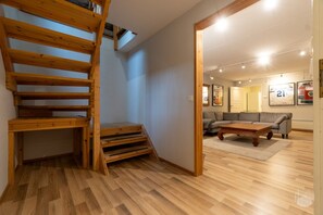 Eine Holztreppe führt zu einer Erkerwohnung, einem Wohnzimmer mit Sofa und Couchtisch, sowie einem Holzboden.