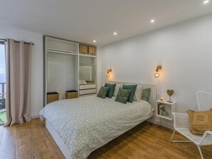 Une chambre à coucher comprenant un lit, une armoire, des tables de chevet, une chaise et une vue sur l’extérieur.