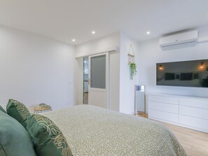 Ein Schlafzimmer mit einem Bett, einem an der Wand montierten Fernseher und einer Tür zu einem anderen Raum.
